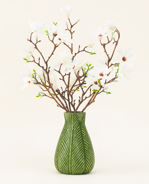 Un vaso verde mostra il bouquet di fiori artificiali in seta Magnolia bianca, con diversi rami di magnolia bianca con piccole foglie verdi, su uno sfondo chiaro.