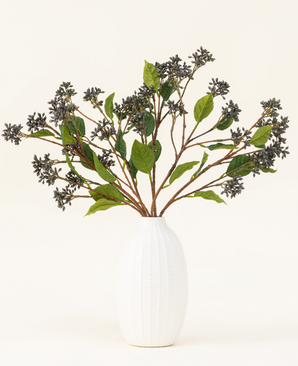 Un bouquet di fiori artificiali in seta Japanese Berry Steel Blue con steli lunghi, bacche viola scuro e foglie in acciaio si trova in un vaso con trama bianca su uno sfondo chiaro.