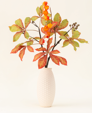 Il bouquet di fiori artificiali in seta Autumn Flair è composto da un vaso con struttura bianca e ramo di lanterna, fiori arancioni a forma di lanterna e foglie verde-rosse, che formano un elegante spettacolo autunnale su uno sfondo chiaro e semplice.