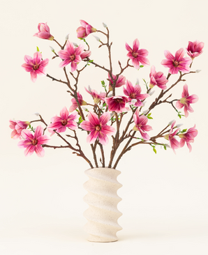 Il bouquet di fiori artificiali in seta Magnolia rosa è disposto in un vaso ondulato in ceramica bianca con boccioli verdi, creando un elegante display su uno sfondo chiaro.