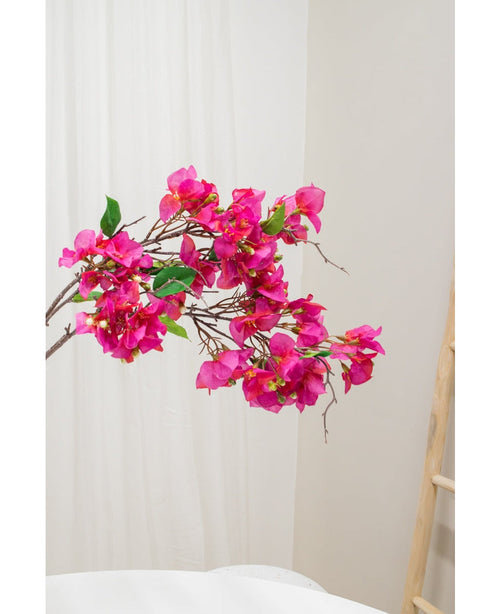 Il fiore artificiale Bougainvillea viola da 90 cm, con vivaci fiori viola e foglie verdi, è mostrato su uno sfondo neutro chiaro accanto a una scala di legno sulla destra.