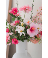 Il fiore artificiale Margriet 60 cm bianco/rosa, un vaso bianco con margherite artificiali rosa e bianche, si trova su uno sfondo chiaro e neutro.