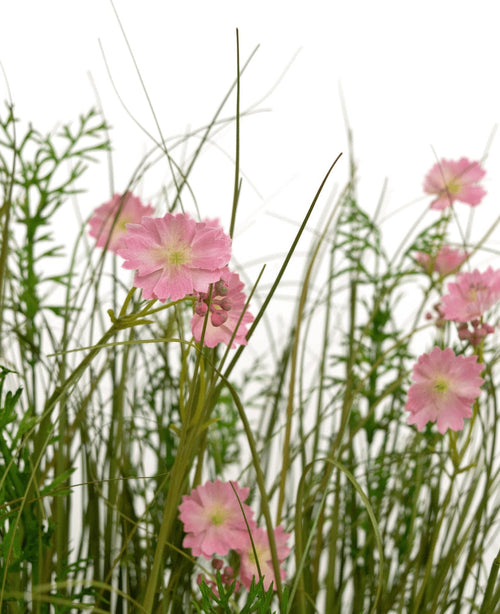 L'erba artificiale rosa Gesang Flower Cipolla in vaso ignifugo da 90 cm ha fiori rosa con un cuore verde chiaro che sbocciano tra erba alta e sottile e piante dal fogliame rigoglioso, il tutto su uno sfondo bianco.