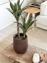 Una pianta di Agave artificiale di 76 cm, con due lunghi steli e foglie verdi e appuntite, si trova su un tavolino in legno in un accogliente soggiorno con un divano color crema, un tavolino rotondo e un arredamento neutro.