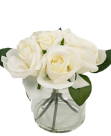 Il bouquet di rose artificiali Real Touch White da 18 cm è un piccolo vaso in vetro trasparente con rose bianche realistiche e foglie verdi, su un semplice sfondo bianco.
