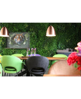Una moderna sala da pranzo con sedie verdi e color pesca, un tavolo decorato con vasi di fiori viola, lampade a sospensione in rame, una rigogliosa parete vegetale realizzata con il pannello Kunsthaag Crush UV di 100 x 100 cm e un'immagine incorniciata di una tigre sullo sfondo.