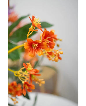 Primo piano del ramo artificiale Daphne Spray da 108 cm in arancione vibrante, con foglie verdi realistiche e stami gialli, su uno sfondo leggermente sbiadito.