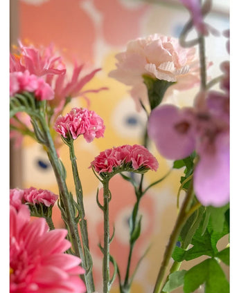 Un primo piano dei fiori artificiali rosa Artificial Statice da 64 cm, caratterizzati da delicati fiori statice rosa su uno sfondo sfocato pastello con forme astratte gialle e pesca.