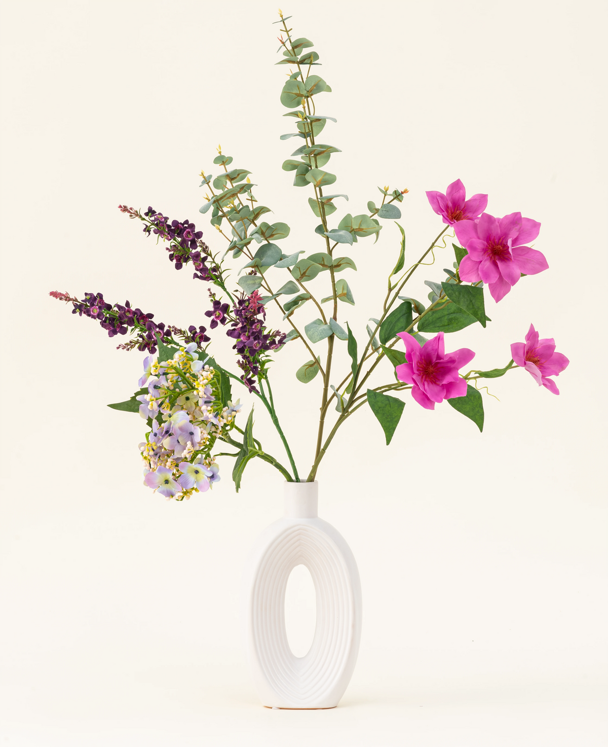 Disposto in un moderno vaso bianco, il bouquet di fiori artificiali in seta Lavender Skies presenta fiori artificiali rosa e viola, accenti gialli e fogliame verde lussureggiante: bellissimo su uno sfondo chiaro e semplice.