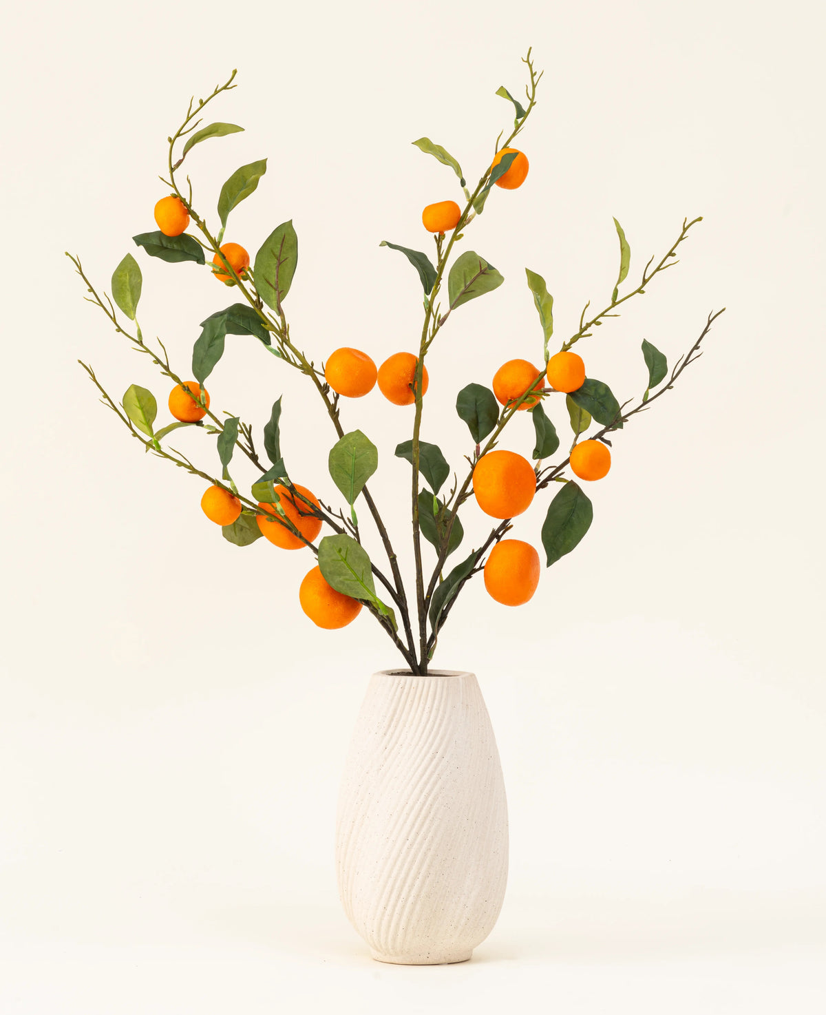 Il bouquet di fiori artificiali in seta Mandarino ha un vaso bianco strutturato e rami di foglie verdi e mandarini artificiali di colore arancione vibrante, che aggiungono un tocco vivace su uno sfondo chiaro e semplice.