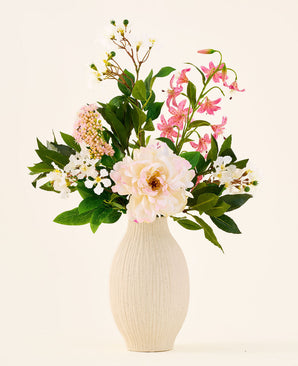 In un vaso di ceramica color crema si trova il bouquet "Light & Lovely" con fiori di seta artificiale di Easyplants, composto da una composizione mista di fiori di seta bianchi, rosa e viola chiaro con foglie verdi, su uno sfondo semplice e chiaro.