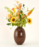 Een vaas met bruine structuur toont het Zijden kunstbloemen boeket Amber Light, met zonnebloemen, witte en oranje bloemen en groen gebladerte tegen een effen achtergrond.