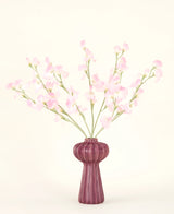 Het Zijden kunstbloemen boeket Erwt lichtroze, met meerdere lichtroze erwt stelen in een geribbelde bordeauxrode vaas, staat tegen een bleke achtergrond - ideaal voor elk kunstbloemen interieur.