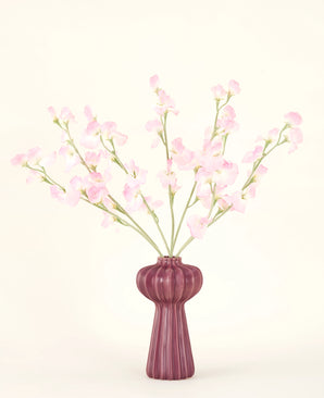 Il bouquet di fiori artificiali in seta Pea rosa chiaro, con diversi steli di pisello rosa chiaro in un vaso bordeaux a coste, si staglia su uno sfondo chiaro - ideale per qualsiasi interno di fiori artificiali.