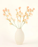 De crèmekleurige vaas van keramiek bevat het Zijden kunstbloemen boeket Erwt perzik, met delicate perzik- en lichtroze bloemen met lange groene stelen tegen een lichte, neutrale achtergrond.