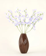 Een bruine, geribbelde vaas bevat het Zijden kunstbloemen boeket Erwt lavendel, met delicate bloemblaadjes en groene stelen tegen een effen gebroken witte achtergrond voor een subtiele cottage sfeer.
