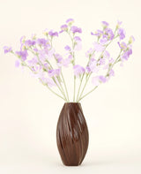 Een bruine vaas met textuur bevat het Zijden kunstbloemen boeket Erwt paars-lichtpaarse zijden bloemen met groenachtige stelen tegen een effen, lichte achtergrond.