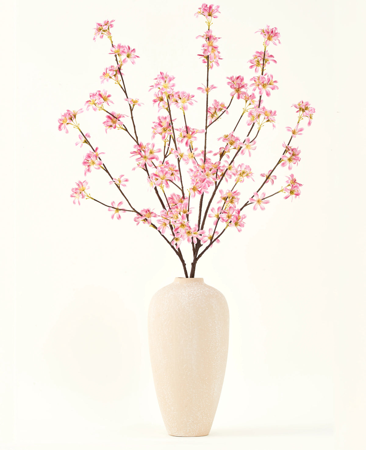 Un vaso alto in ceramica beige contiene diversi rami del bouquet di fiori artificiali in seta Fiori rosa, con delicati fiori rosa e foglie verdi, su un semplice sfondo bianco.