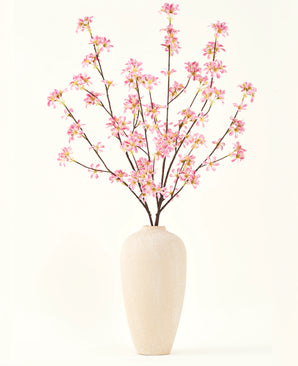Un vaso alto in ceramica beige contiene diversi rami del bouquet di fiori artificiali in seta Fiori rosa, con delicati fiori rosa e foglie verdi, su un semplice sfondo bianco.