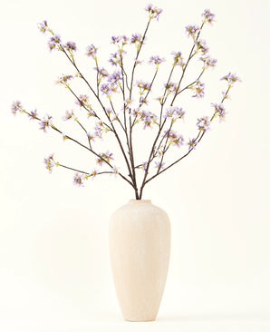 Un vaso alto in ceramica color crema contiene una serie di rami sottili con il testo Bouquet di fiori artificiali in seta Ramo di fiori artificiali viola, su uno sfondo semplice e chiaro.