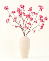 De Zijden kunstbloemen boeket Kersenbloesem fuchsia 114 cm voegt een levendige knal van kleur toe aan je interieur met zijn opvallende takken en fuchsia bloesems, prachtig weergegeven in een beige keramische vaas tegen een effen gebroken witte achtergrond.