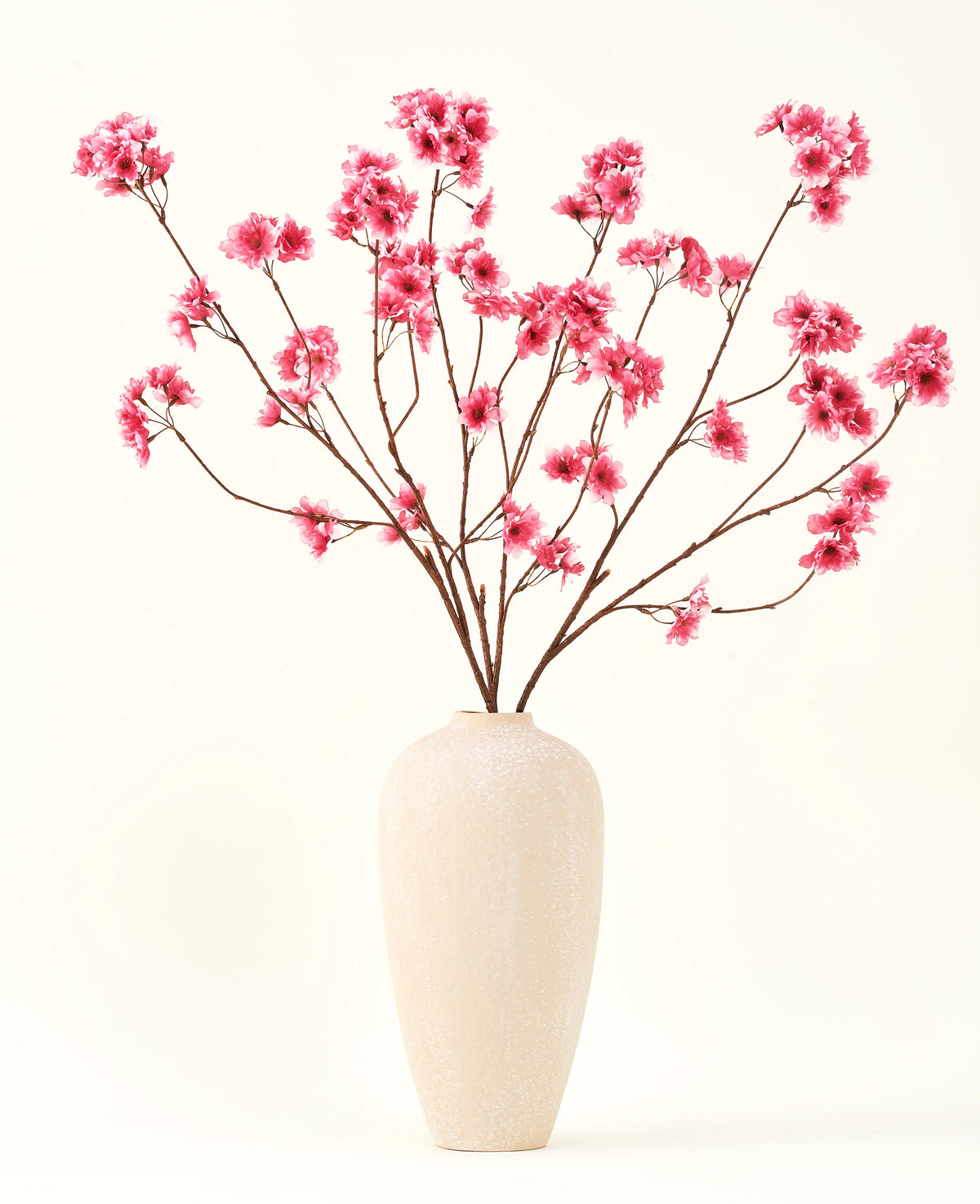 Il bouquet di fiori artificiali in seta Fiore di ciliegio fucsia 114 cm aggiunge un vivace tocco di colore ai tuoi interni con i suoi rami sorprendenti e fiori fucsia, splendidamente esposti in un vaso di ceramica beige su un semplice sfondo bianco sporco.