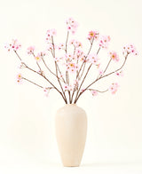 Het Zijden kunstbloemen boeket Kersenbloesem roze 114 cm heeft lange, dunne takken met trossen lichtroze bloemen in een beige vaas van keramiek, die een opvallend contrast vormen tegen de effen witte achtergrond.