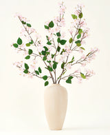 Een beige vaas van keramiek bevat verschillende lange takken met het Zijden kunstbloemen boeket Perzikbloesem roze en groene bladeren, tegen een effen witte achtergrond - perfect voor een kunstbloemen interieur.
