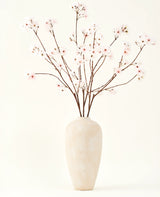 De Zijden kunstbloemen boeket Kersenbloesem blush 114 cm heeft hoge, delicate takken in een eenvoudige beige vaas, die een zachte, elegante touch toevoegt aan je interieur tegen een effen, lichte achtergrond.