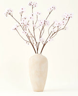 De Zijden kunstbloemen boeket Kersenbloesem lichtroze 114 cm staat in een hoge vaas van beige keramiek met lange, dunne takken en delicate lichtroze bloemen, waardoor een sereen kunstbloemen accent ontstaat tegen een effen achtergrond.
