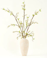 Een hoge, crèmekleurige vaas van keramiek bevat het Zijden kunstbloemen boeket Verbena crème met lange takken, kleine groene blaadjes en delicate witte bloesems, prachtig gerangschikt tegen een effen lichte achtergrond.