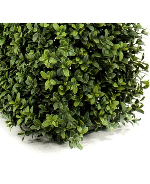 Primo piano delle fitte foglie verdi della Siepe di Bosso Artificiale UV 70x20x25 cm che forma una rigogliosa siepe artificiale con piccole foglie rotonde in diverse tonalità. In basso a sinistra è visibile uno spesso angolo quadrato.