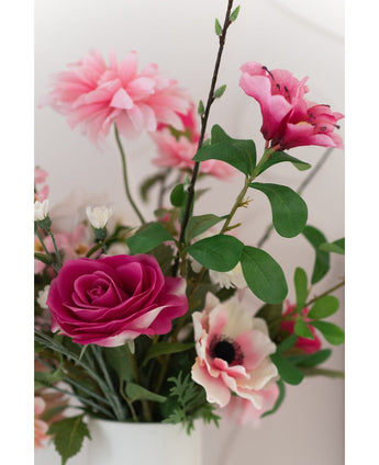 Een close-up van de Kunstroos Real Touch 56 cm roze, een boeket van roze kunstrozen met groene bladeren in een witte vaas, tegen een lichte achtergrond.