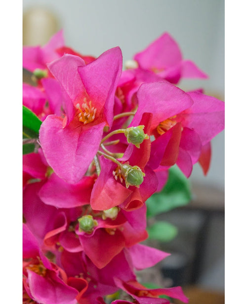 Un primo piano del fiore artificiale Bougainvillea viola da 90 cm mostra vivaci fiori artificiali viola con boccioli verdi su uno sfondo leggermente sfocato.