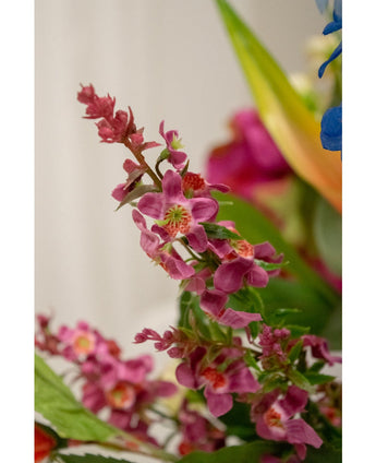 Close-up van Kunstbloem Kattenkruid 75 cm roze: een cluster felroze kunstbloemen met een groen hart en weelderige bladeren, scherp afgebeeld tegen een zacht vage achtergrond met vleugjes van andere bloemen.
