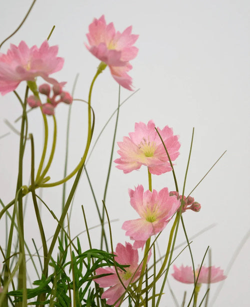 L'erba artificiale rosa Gesang Flower Cipolla in vaso ignifugo da 56 cm ha delicati fiori rosa con sottili steli verdi e foglie strette, disposti su uno sfondo chiaro per un effetto morbido e arioso.