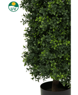 Een close-up van een Kunstplant Buxus Pyramide UV 90 cm met dichte groene bladeren. In de linkerbovenhoek staat een UV-beschermingssymbool met een gele zon en "UV" in een groene cirkel.
