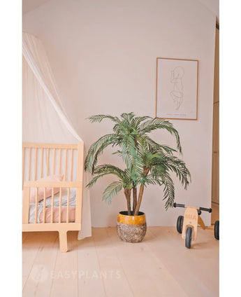 Een gezellige kinderkamer met een licht houten ledikant, de Kunstpalm Cycas Classic 135 cm in een gele plantenbak, een houten speelgoedfiets met het label MIA, minimalistische lijnkunst aan de muur, lichthouten vloeren en zachtroze beddengoed voor extra warmte.