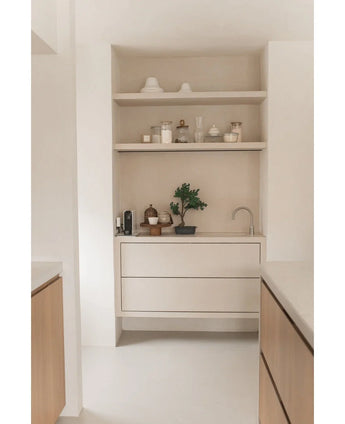 Minimalistische keukenhoek met lichthouten planken met potten, vazen, decor, een aanrecht met kleine apparaten en de Kunstplant Bonsai Juniper 40 cm potplant, plus ingebouwde laden en een kleine kraan - alles in neutrale tinten.
