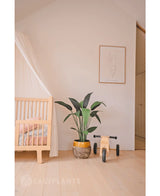 Een minimale kinderkamer met een licht houten wiegje, Kunstplant Heliconia 110 cm, houten speelgoed en eenvoudige muurkunst in een lichte, opgeruimde kamer - perfecte inspiratie voor kleine ruimtes inrichting.
