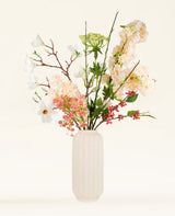 Het Zijden kunstbloemen boeket Springtime Poem, met witte en roze bloemen, groene bladeren en rode bessen in een witte vaas met textuur, wordt weergegeven tegen een lichte achtergrond.