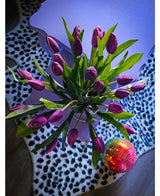 Het Zijden kunstboeket Tulpen in vaas Paars rust op een lavendelkleurige tafel naast een levendige discobal op een zwart-wit vloerkleed met luipaardprint.