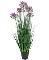 De Kunstgras paarse Agapanthus uiengraspot is een 90 cm hoge, brandvertragende kunstplant met lange groene bladeren en trossen paarse bloemen, weergegeven in een effen zwarte pot tegen een witte achtergrond.