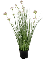 L'erba artificiale bonsai con fiori di porro e cipolla ignifuga da 61 cm ha foglie verdi lunghe e sottili e steli lunghi con piccoli grappoli di fiori viola chiaro, presentati in un vaso su un semplice sfondo bianco.